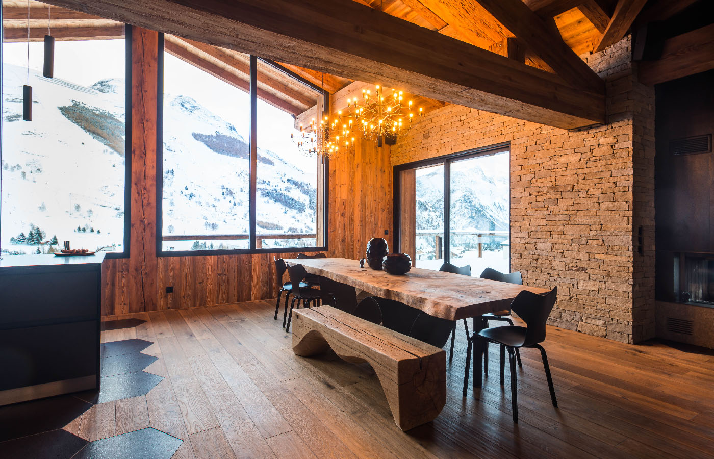 Espace de vie avec cheminée, grande table en chêne sur mesure pour 14 convives, escalier design, et terrasse avec panorama imprenable dans un chalet à louer aux 2 Alpes