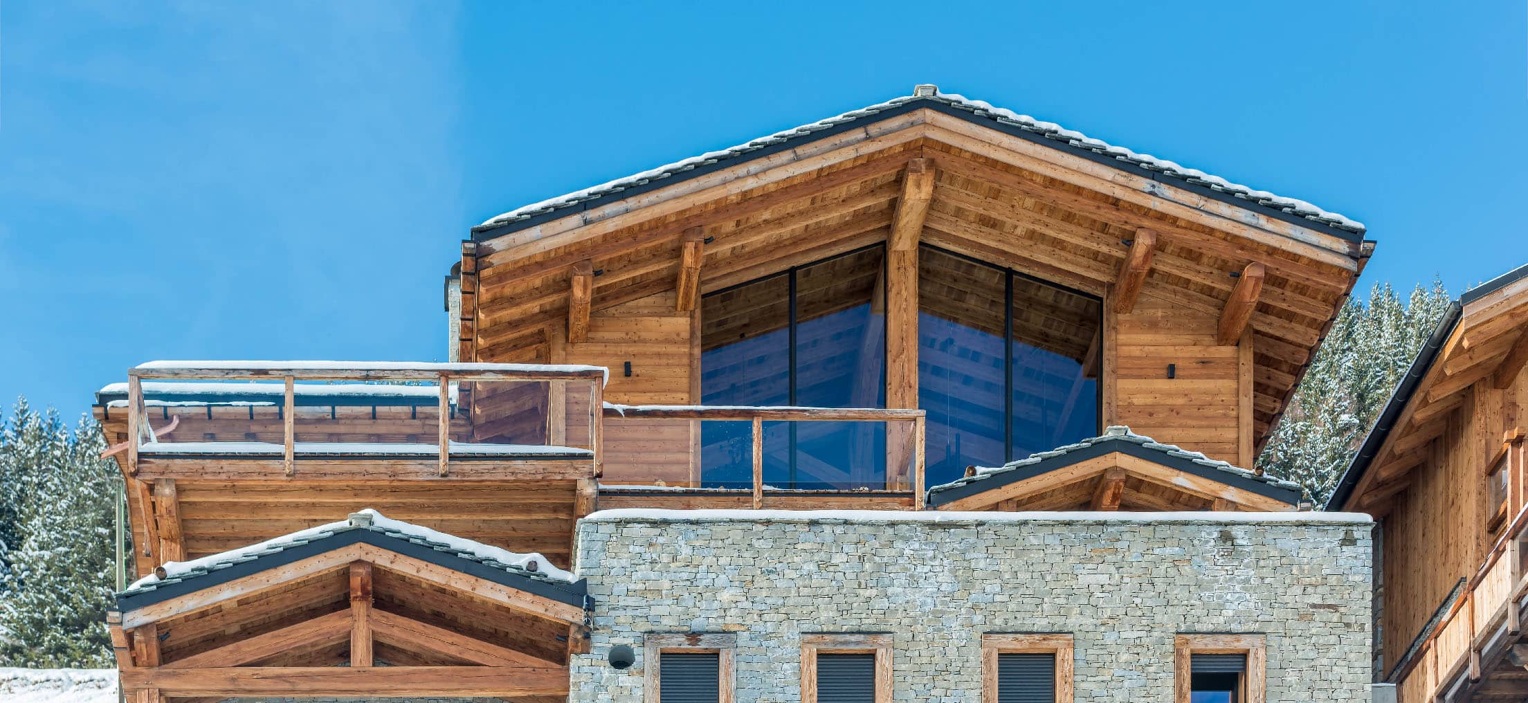 Vue extérieure du chalet avec fenêtres panoramiques et balcon en bois, offrant une vue imprenable sur les montagnes enneigées, location chalet 2 Alpes